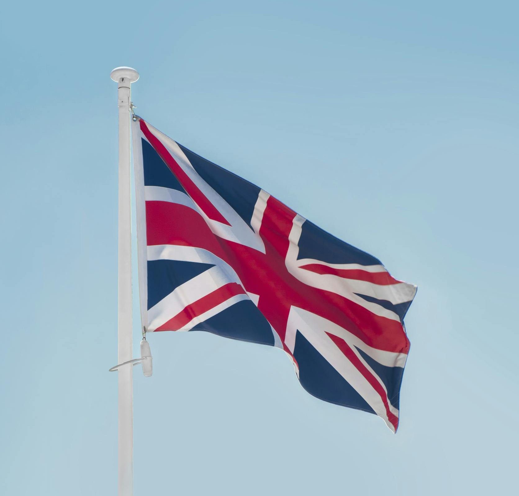 Union Jack flag waving on a flagpole against a clear blue sky in London.